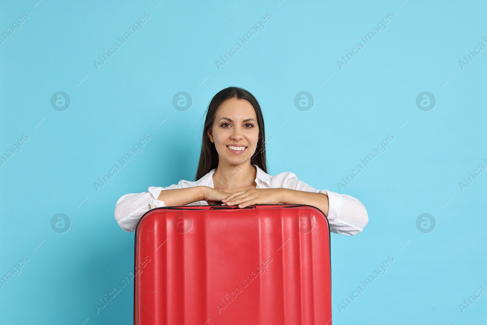 Photo of Happy young woman with suitcase on light blue background