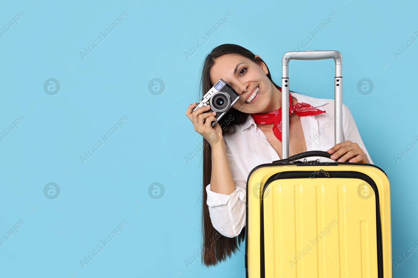 Photo of Happy young woman with suitcase and vintage camera on light blue background, space for text