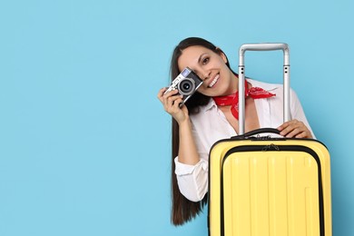 Happy young woman with suitcase and vintage camera on light blue background, space for text