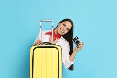 Happy young woman with suitcase and vintage camera on light blue background