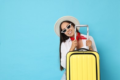 Photo of Happy young woman in sunglasses with suitcase and on light blue background, space for text