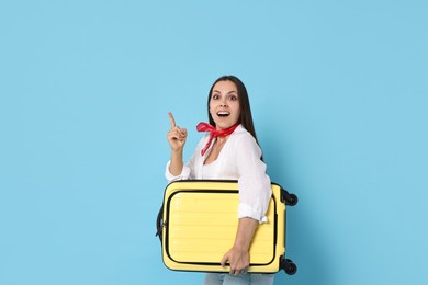 Surprised woman with suitcase pointing at something on light blue background