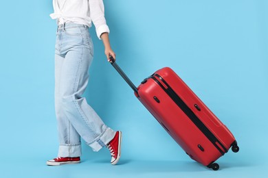 Woman with suitcase on light blue background, closeup