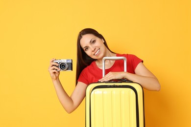 Photo of Happy young woman with suitcase and vintage camera on orange background