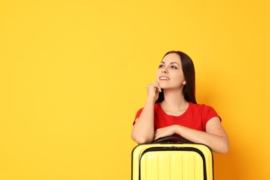 Photo of Happy young woman with suitcase on orange background, space for text