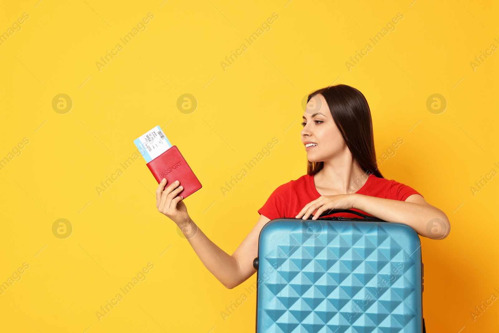 Photo of Happy young woman with suitcase, passport and ticket on orange background