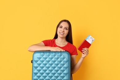 Photo of Happy young woman with suitcase, passport and ticket on orange background