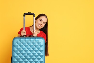 Happy young woman with suitcase on orange background, space for text