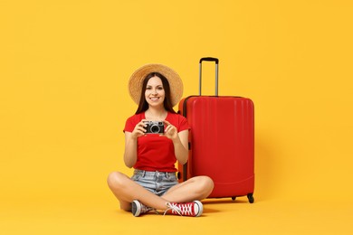 Photo of Happy young woman with vintage camera and suitcase on orange background