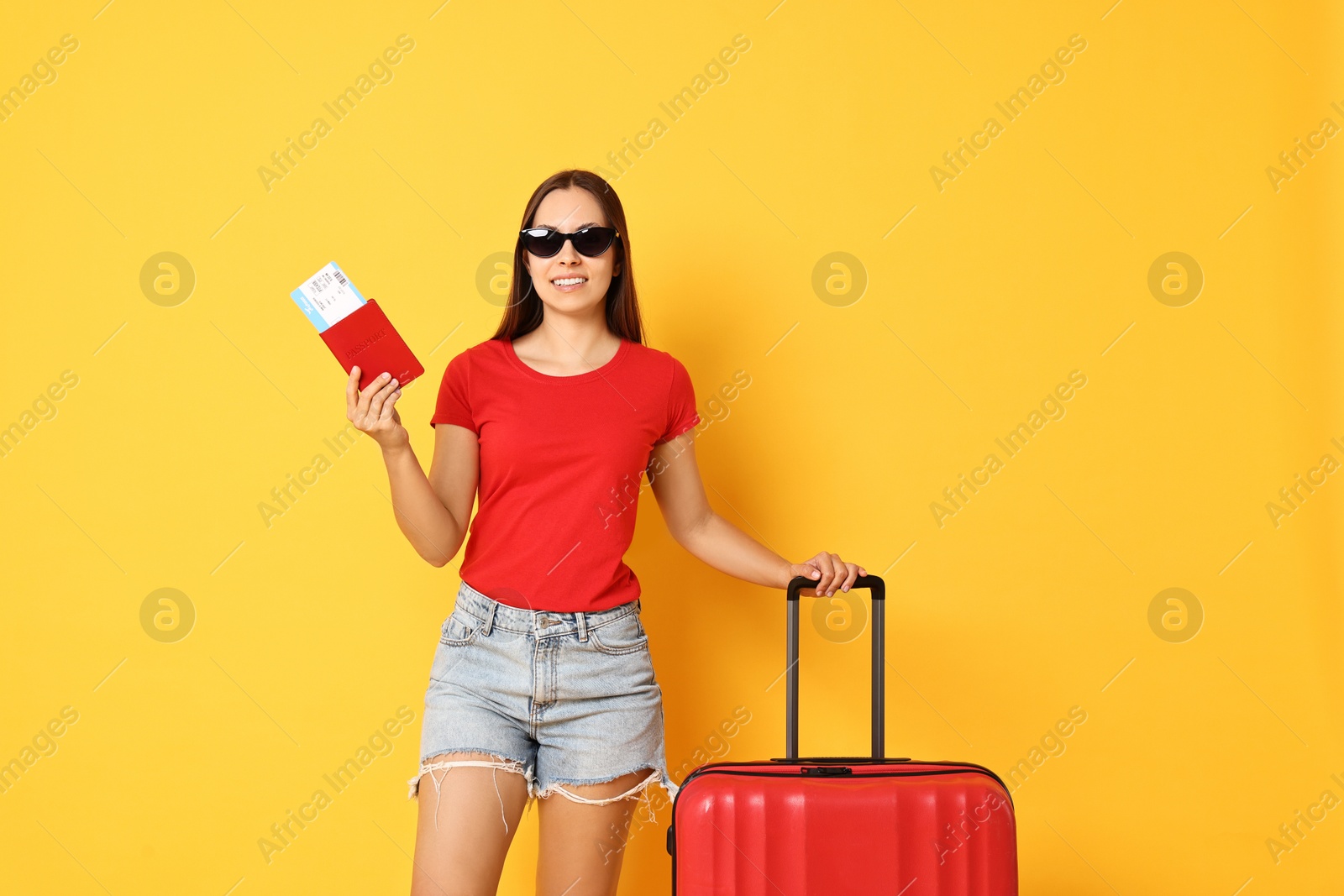 Photo of Happy young woman in sunglasses with suitcase, passport and ticket on orange background