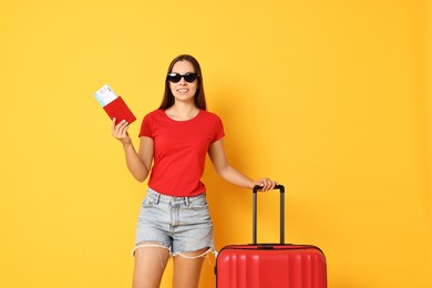 Photo of Happy young woman in sunglasses with suitcase, passport and ticket on orange background