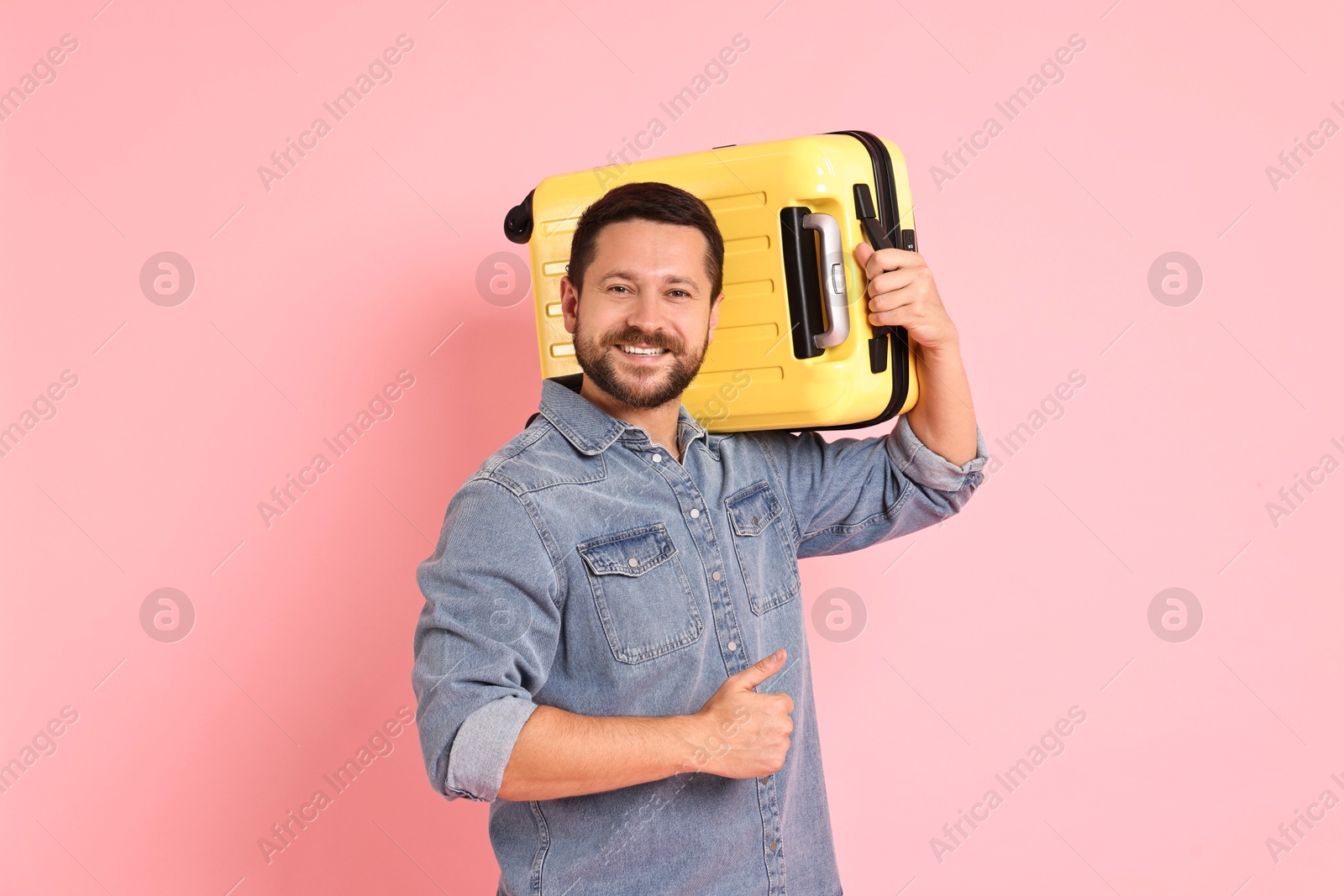 Photo of Happy man with suitcase showing thumbs up on pink background