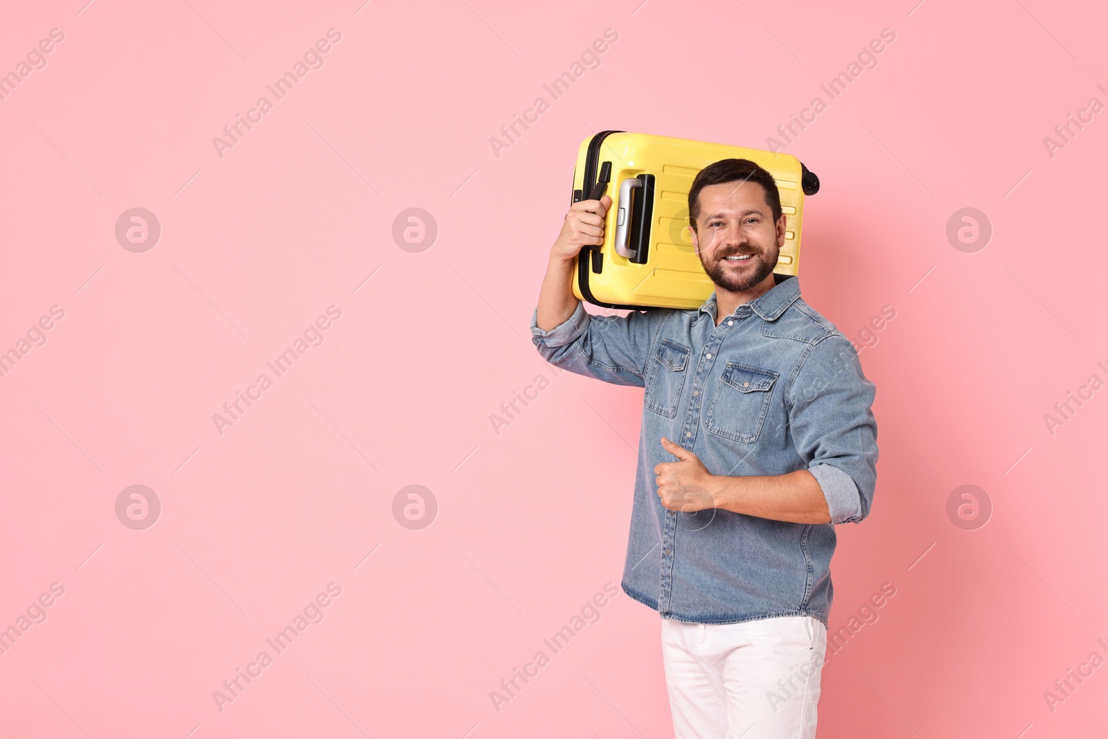 Photo of Happy man with suitcase showing thumbs up on pink background, space for text