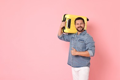 Happy man with suitcase showing thumbs up on pink background, space for text