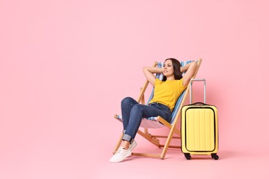 Photo of Happy young woman sitting on folding chair and suitcase against pink background, space for text