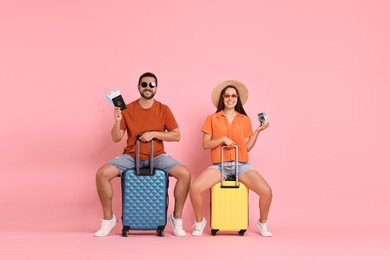 Happy couple with suitcases, passport, tickets and vintage camera on pink background