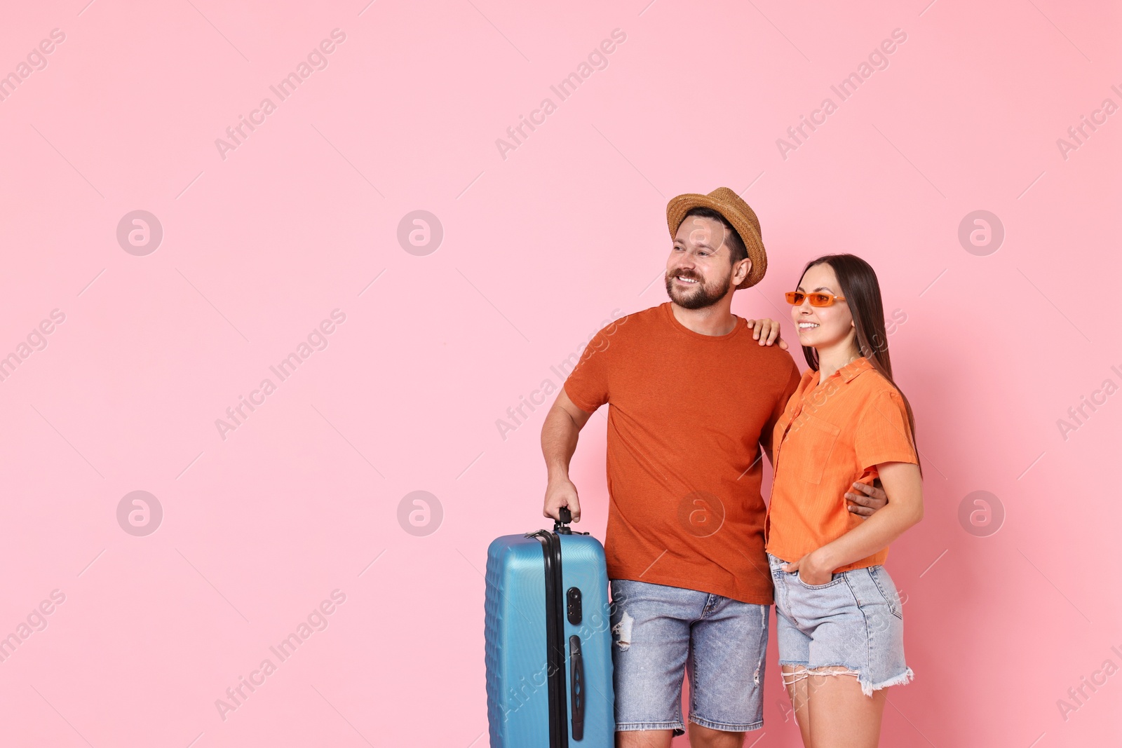 Photo of Happy woman and man with suitcase on pink background, space for text