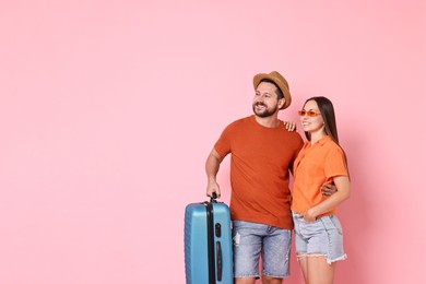 Happy woman and man with suitcase on pink background, space for text