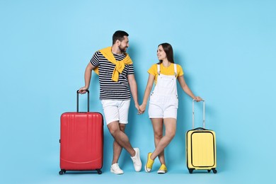 Happy couple with suitcases on light blue background