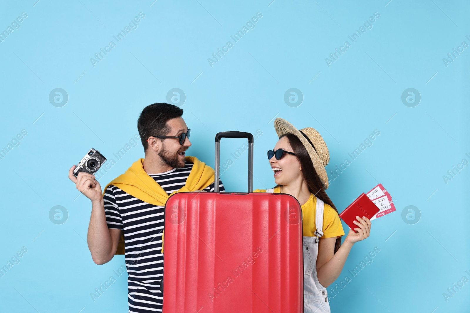 Photo of Happy couple with suitcase, passport, tickets and vintage camera on light blue background