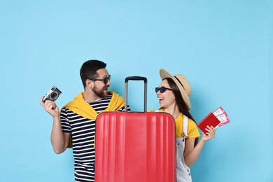 Happy couple with suitcase, passport, tickets and vintage camera on light blue background