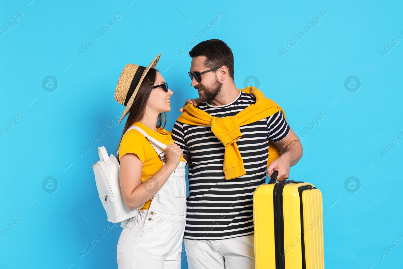 Photo of Happy couple with suitcase on light blue background