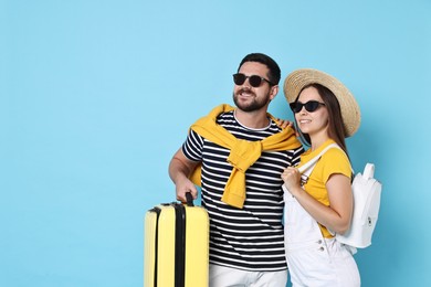 Happy man with suitcase and woman on light blue background, space for text