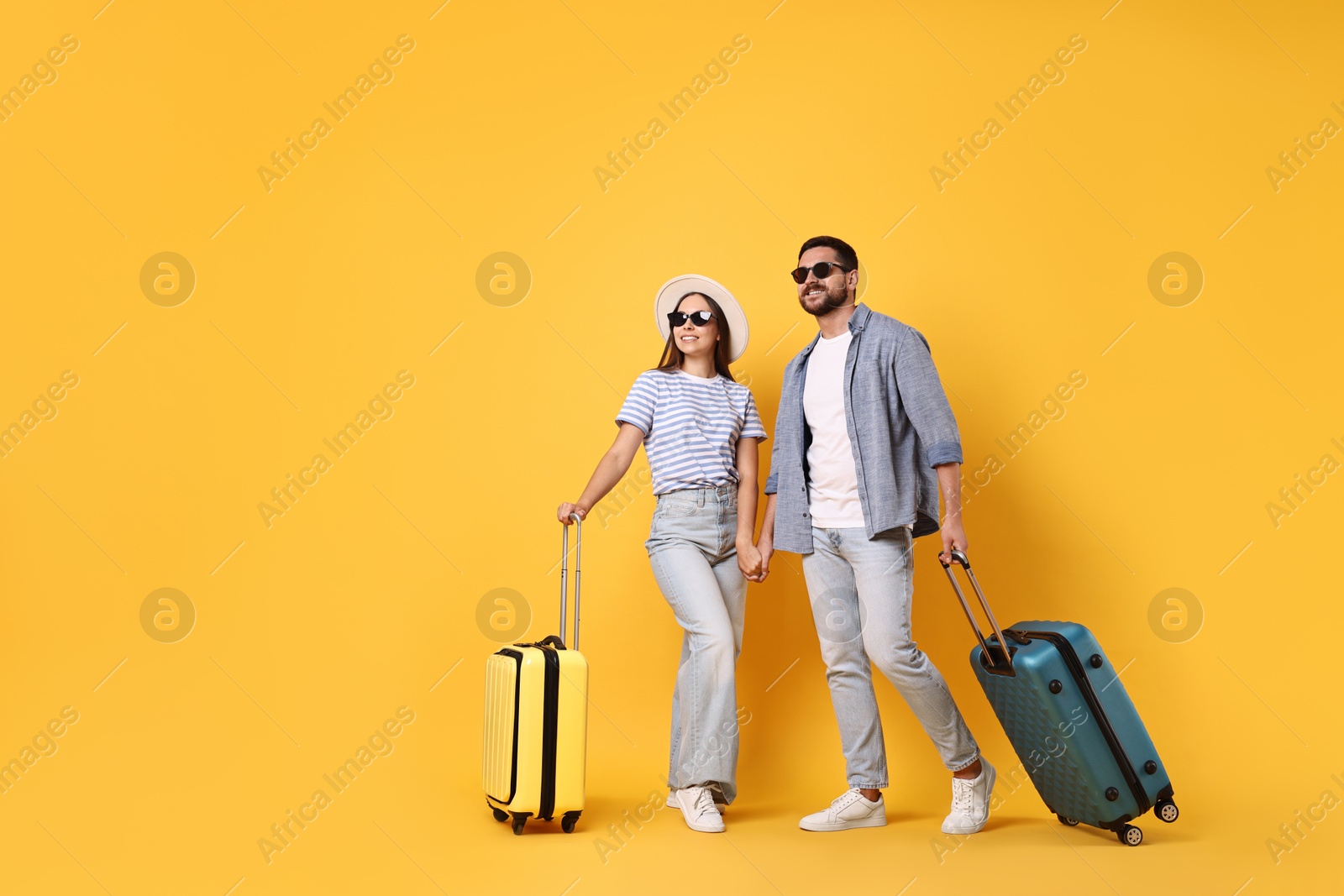 Photo of Happy couple in sunglasses with suitcases on orange background