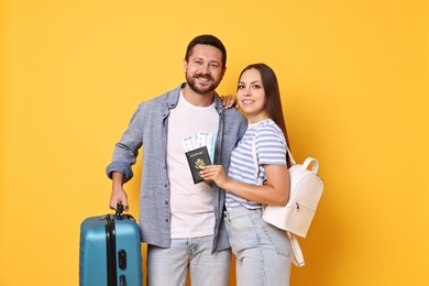 Happy couple with suitcase, passport and tickets on orange background