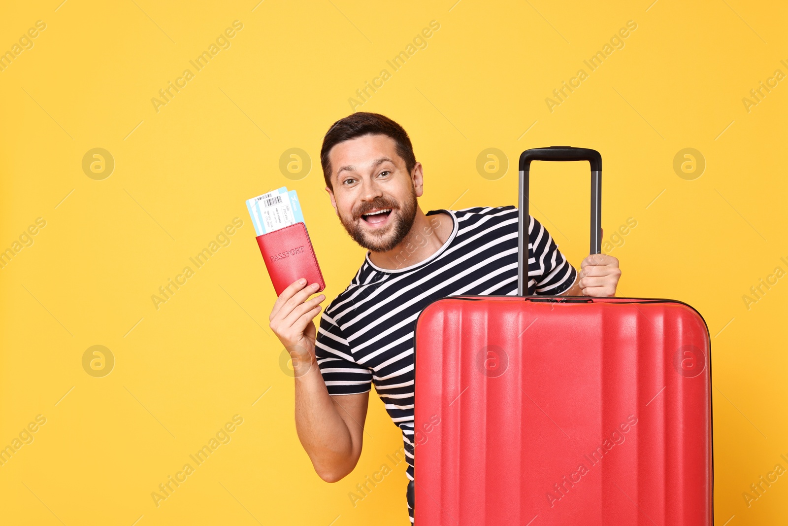 Photo of Happy man with passport, tickets and suitcase on orange background