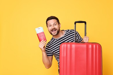 Happy man with passport, tickets and suitcase on orange background