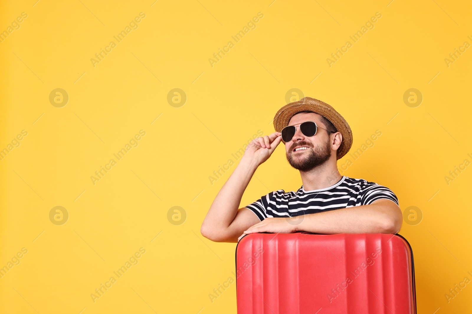 Photo of Happy man in sunglasses with suitcase on orange background, space for text