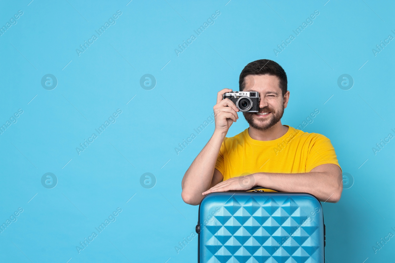 Photo of Happy man with suitcase and vintage camera on light blue background, space for text