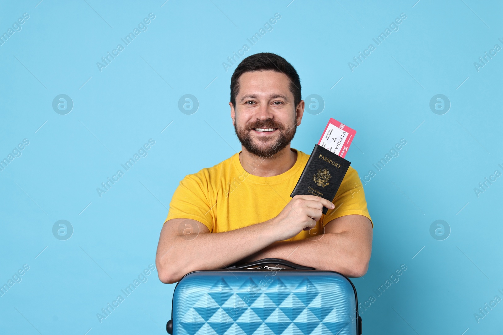 Photo of Happy man with suitcase, passport and ticket on light blue background