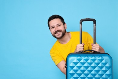 Photo of Happy man with suitcase on light blue background, space for text