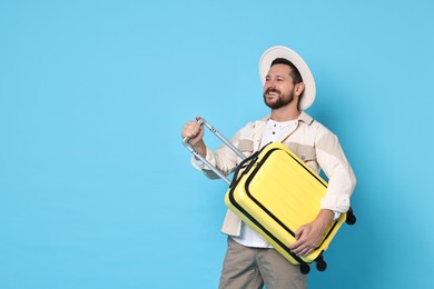 Happy man with suitcase on light blue background, space for text