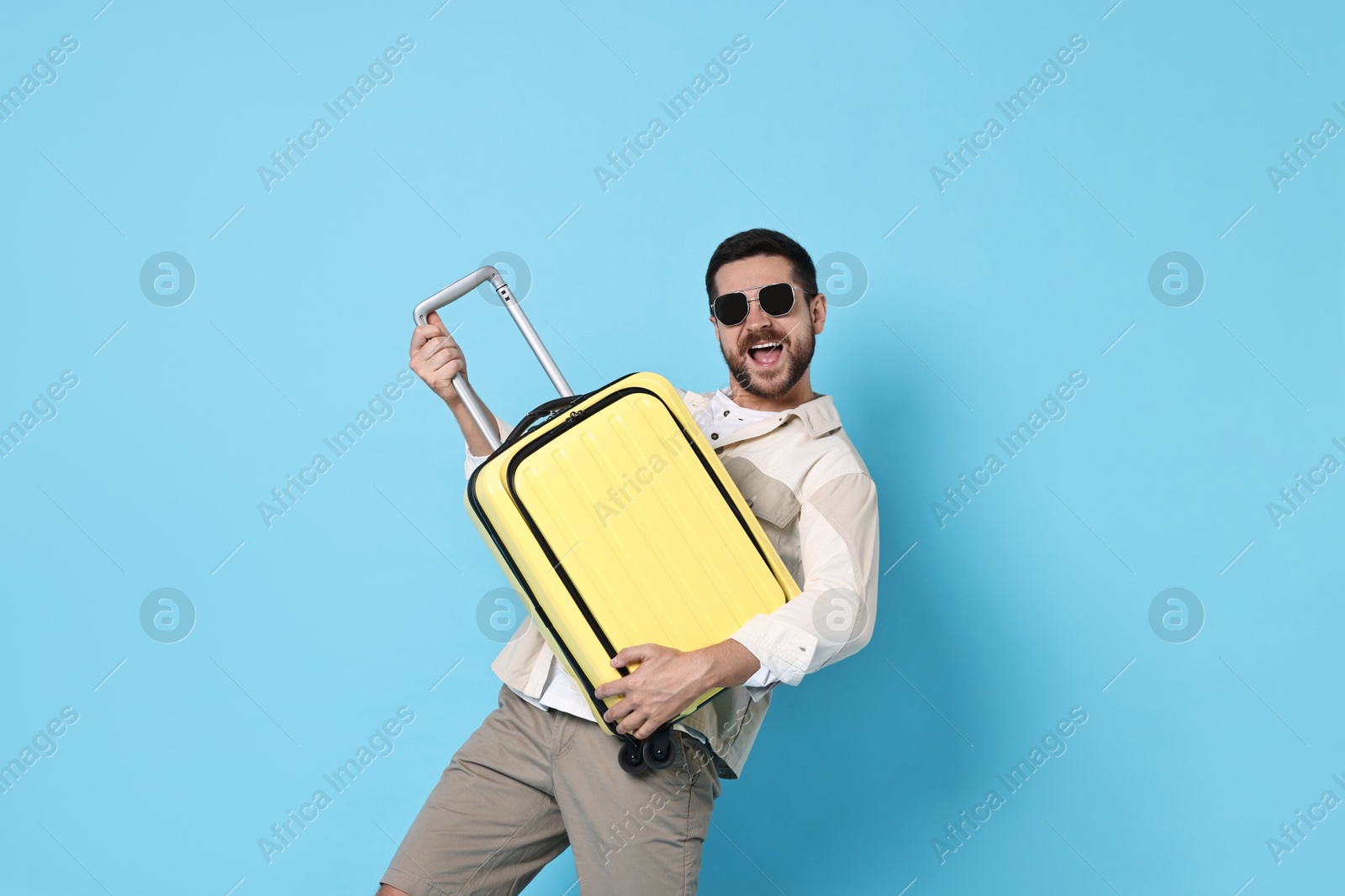 Photo of Happy man in sunglasses with suitcase on light blue background