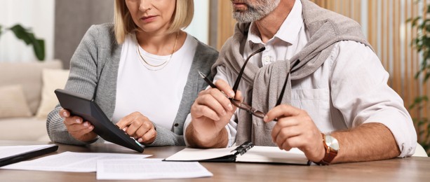 Photo of Pension savings. Couple planning budget at wooden table indoors, closeup