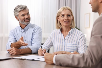 Photo of Pension plan. Couple consulting with insurance agent at table indoors