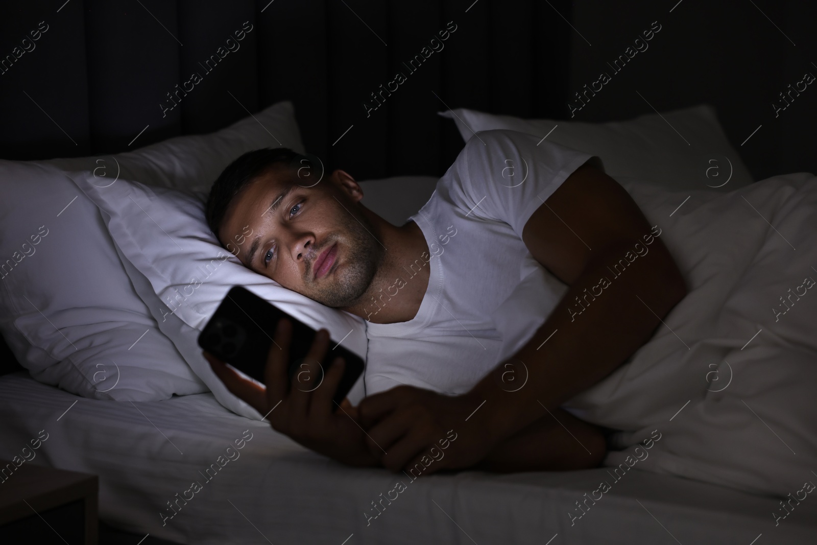 Photo of Bad habit. Man using smartphone in bed at night