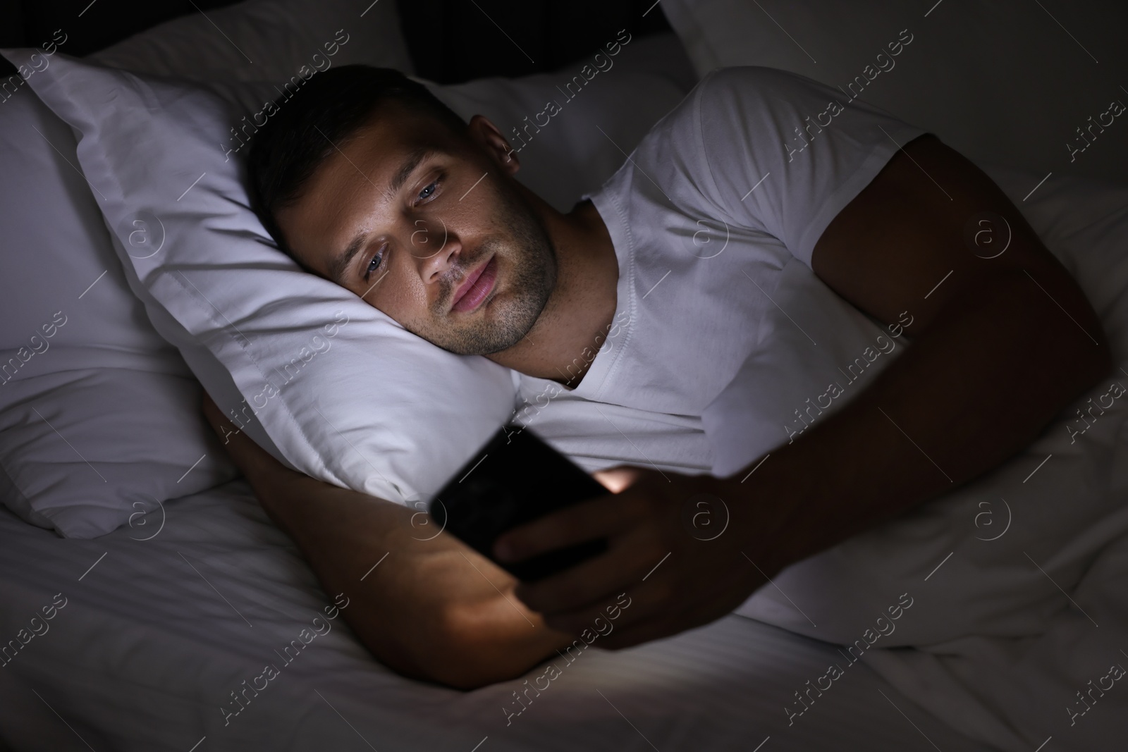 Photo of Bad habit. Man using smartphone in bed at night