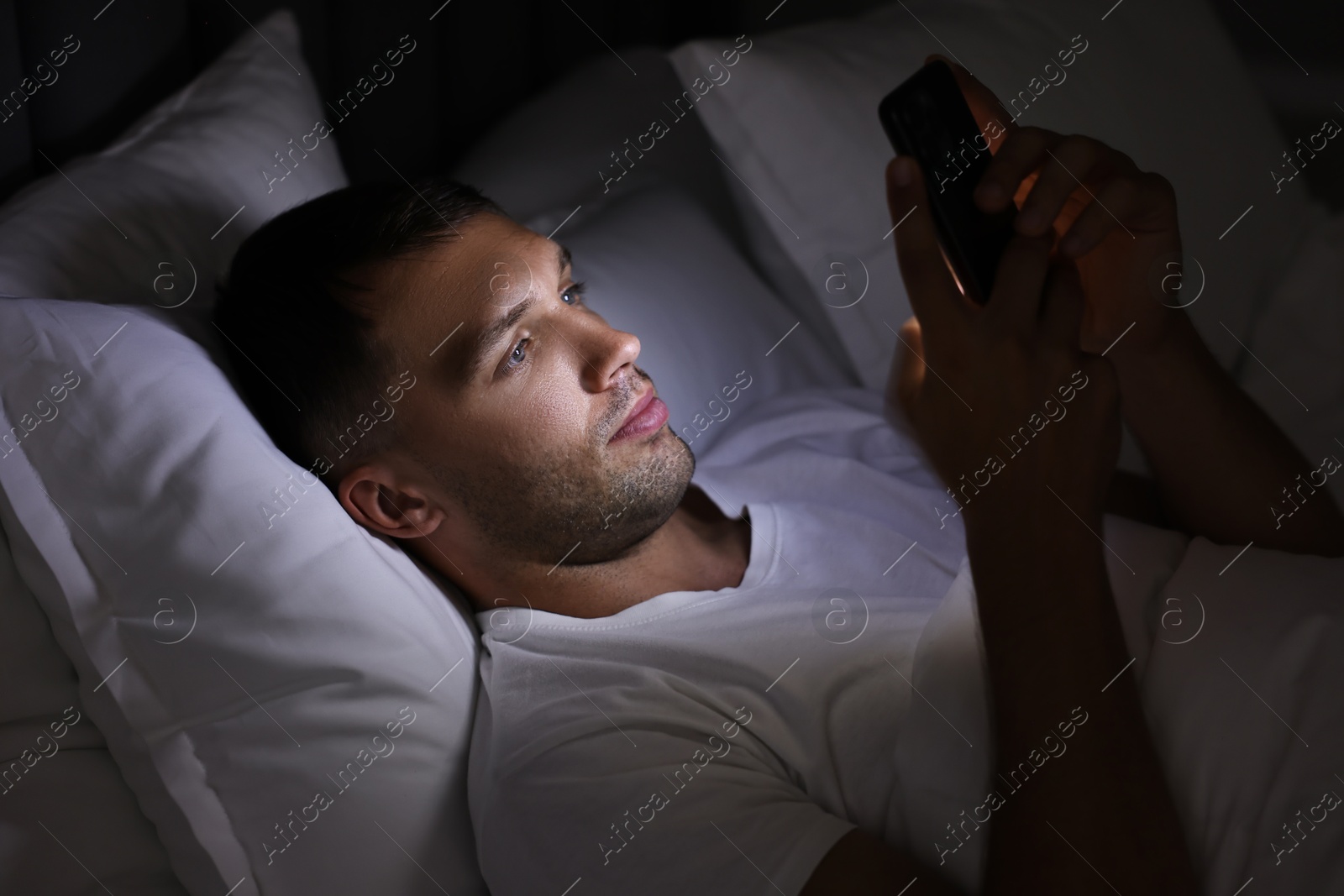 Photo of Bad habit. Man using smartphone in bed at night