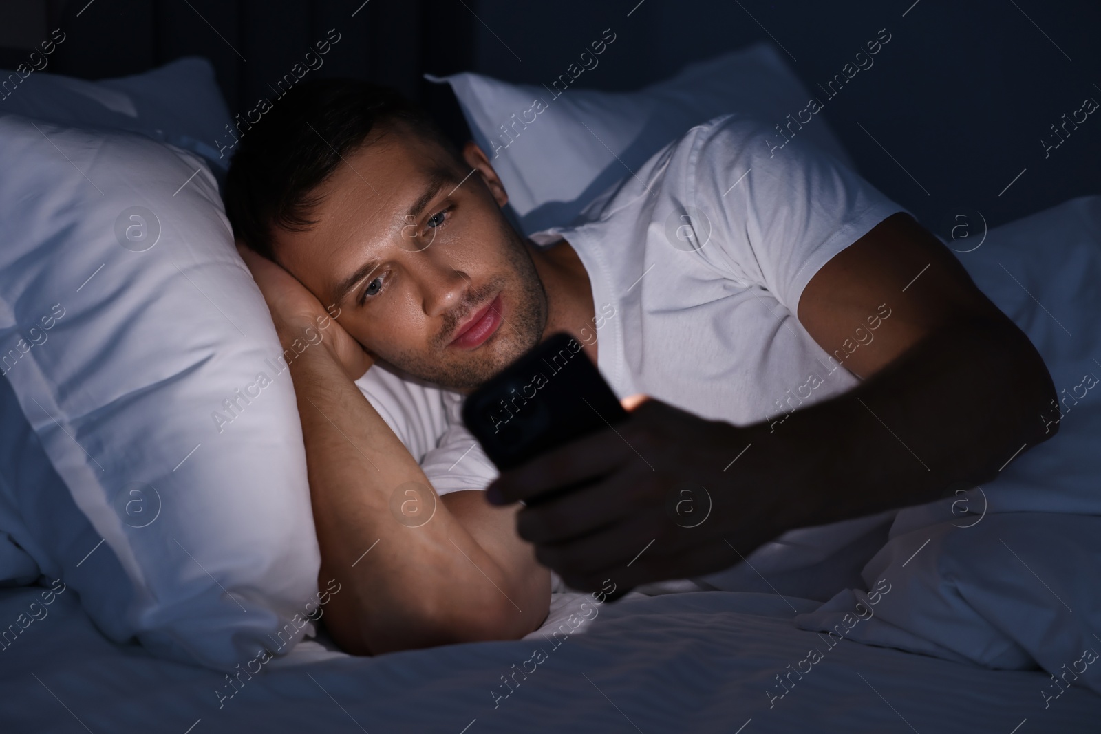 Photo of Bad habit. Man using smartphone in bed at night