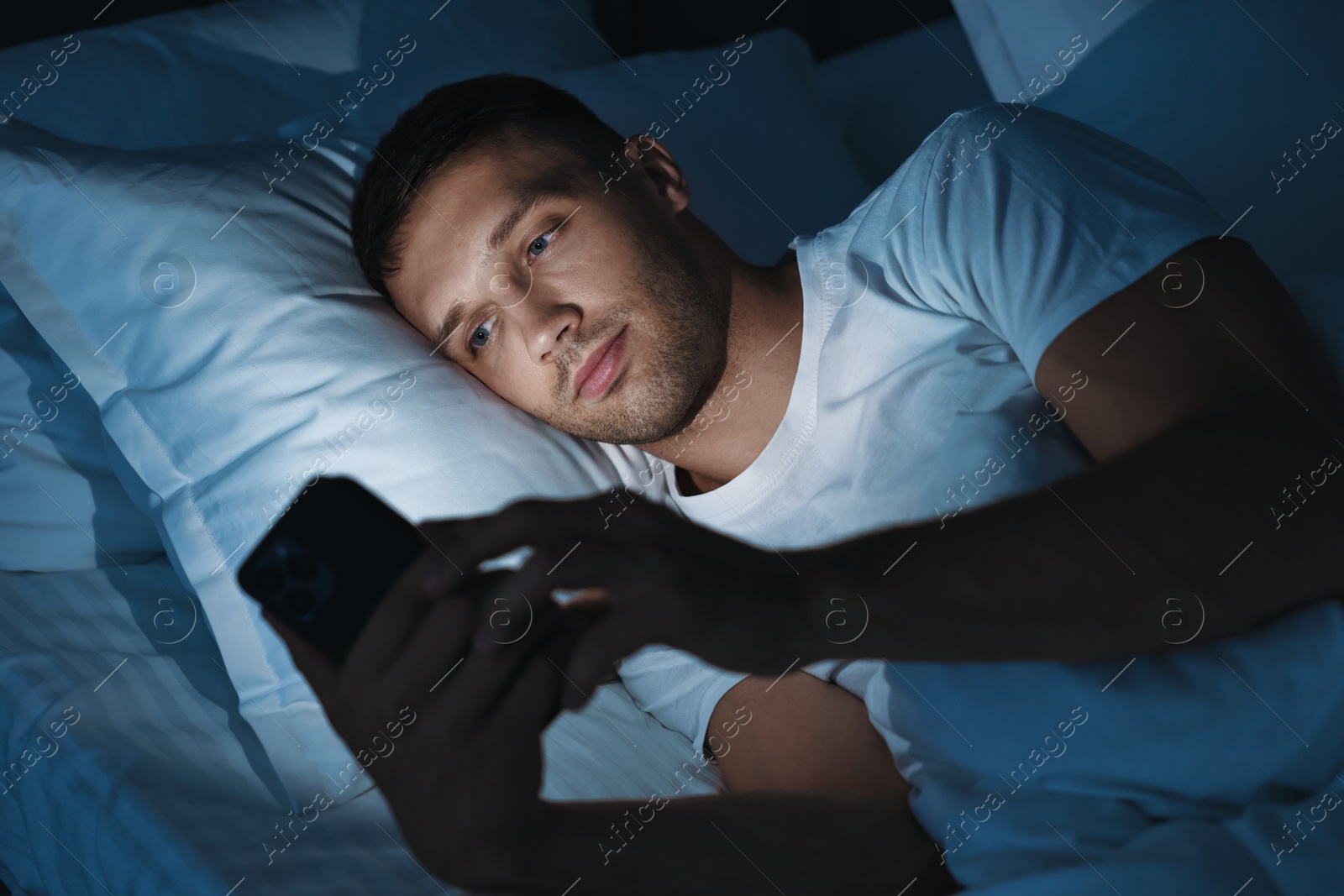 Photo of Bad habit. Man using smartphone in bed at night