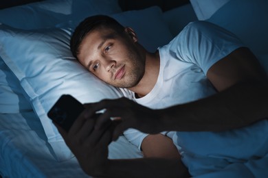 Bad habit. Man using smartphone in bed at night