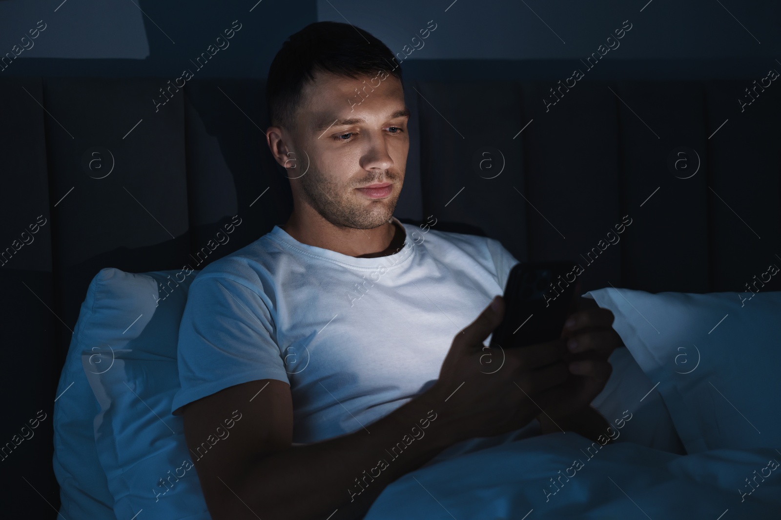 Photo of Bad habit. Man using smartphone in bed at night