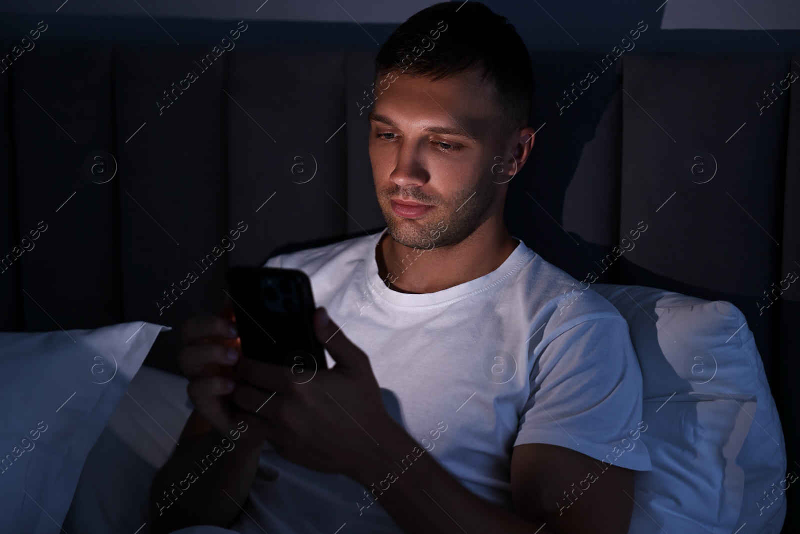 Photo of Bad habit. Man using smartphone in bed at night