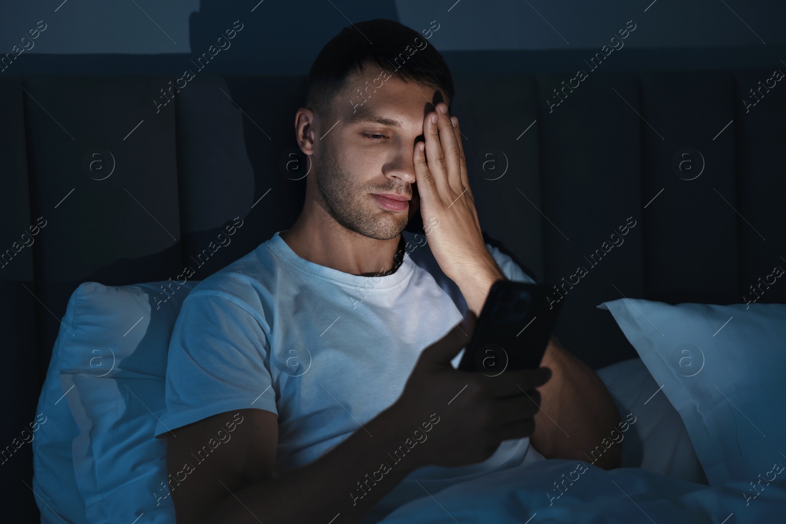 Photo of Bad habit. Sleepy man using smartphone in bed at night