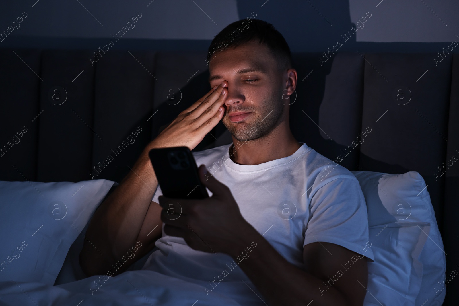 Photo of Bad habit. Sleepy man using smartphone in bed at night