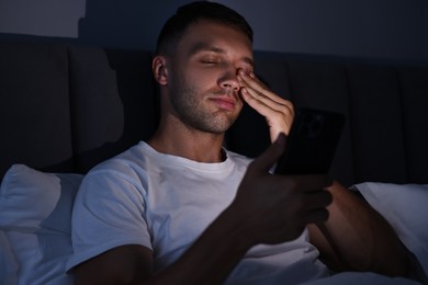 Photo of Bad habit. Sleepy man using smartphone in bed at night